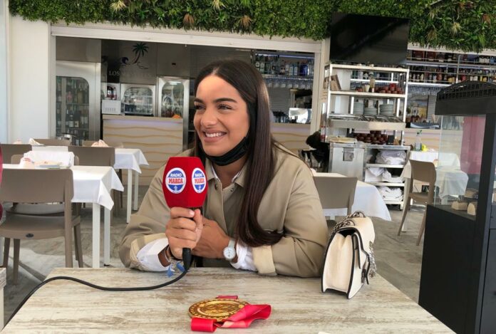 María Torres sujeta el micrófono rojo, acompañada de la medalla de oro.